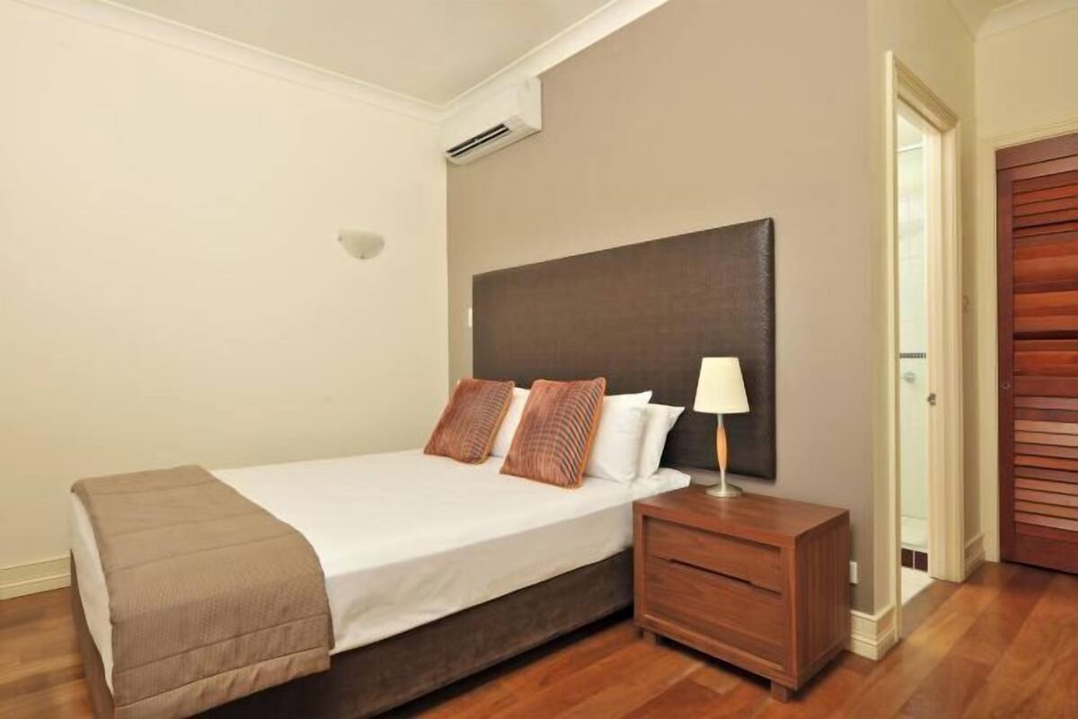 Un dormitorio con cama, mesita de noche y puerta de madera.