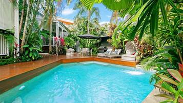 A pool area with lounge chairs and umbrellas, surrounded by tropical plants.