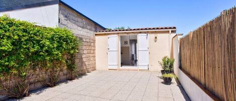 A courtyard with a building featuring a tiled floor, a wooden fence, and a small garden area with potted plants.