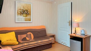 Ett rum med en soffa, en tavla, en dörr, en lampa och ett litet bord med en vattenkokare.