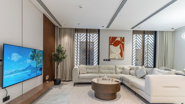 A modern living room with a sectional sofa, a coffee table, a flat-screen TV, and a large window with curtains. - Fancy hosting (Riyadh)