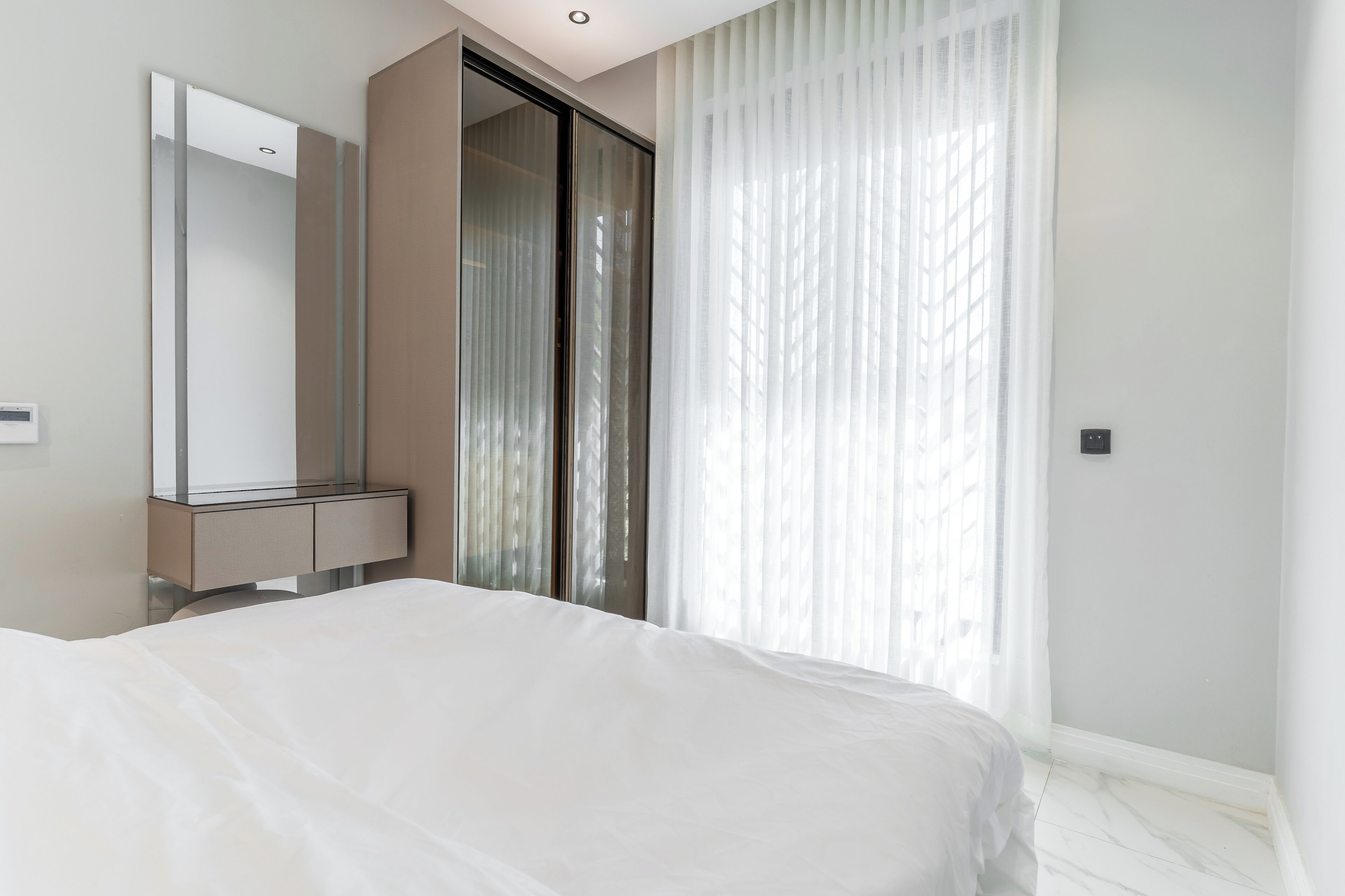 A modern bedroom with a large bed, a built-in wardrobe, and a large window with sheer curtains.