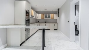 A modern kitchen with white cabinetry, a central island, and a marble floor. - Fancy hosting (Riyadh)