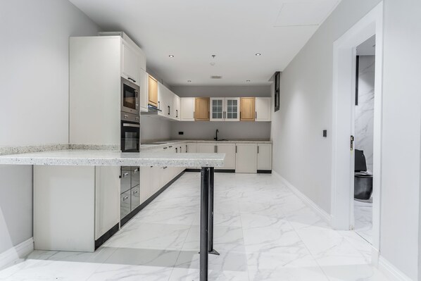A modern kitchen with white cabinetry, a central island, and a marble floor. - Fancy hosting (Riyadh)