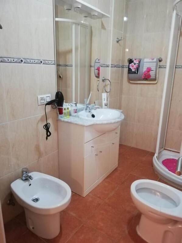 A bathroom with a sink, two bidets, a mirror, and a towel rack with floral decorations.