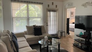 A living room with a sofa, a glass coffee table, a TV, and a bookshelf.