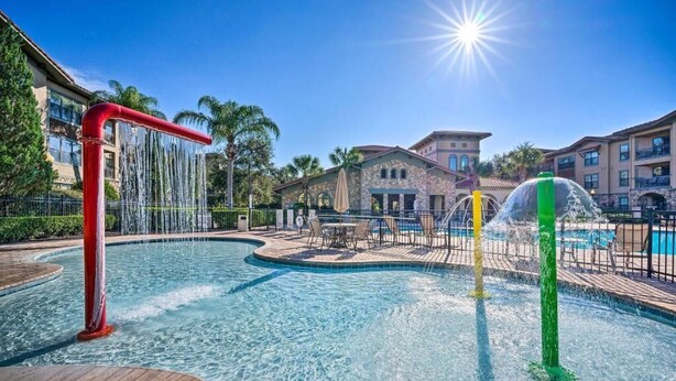 A swimming pool with water features, a patio area, and a building in the background.
