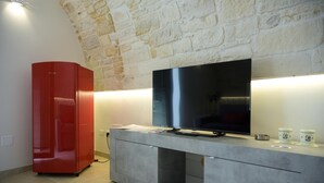 Una sala de estar moderna con pared de piedra, un mueble rojo, un televisor de pantalla plana y una vitrina de vidrio.