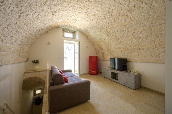 Una sala de estar acogedora con techo de piedra, un sofá, un mueble rojo y un televisor.