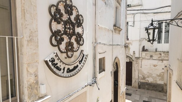 Un estrecho callejón con un edificio que tiene un letrero de metal decorativo y una reja de hierro forjado.