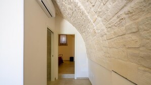 Un pasillo estrecho con una pared de piedra a un lado y una puerta que da a una habitación con cama y ventana.