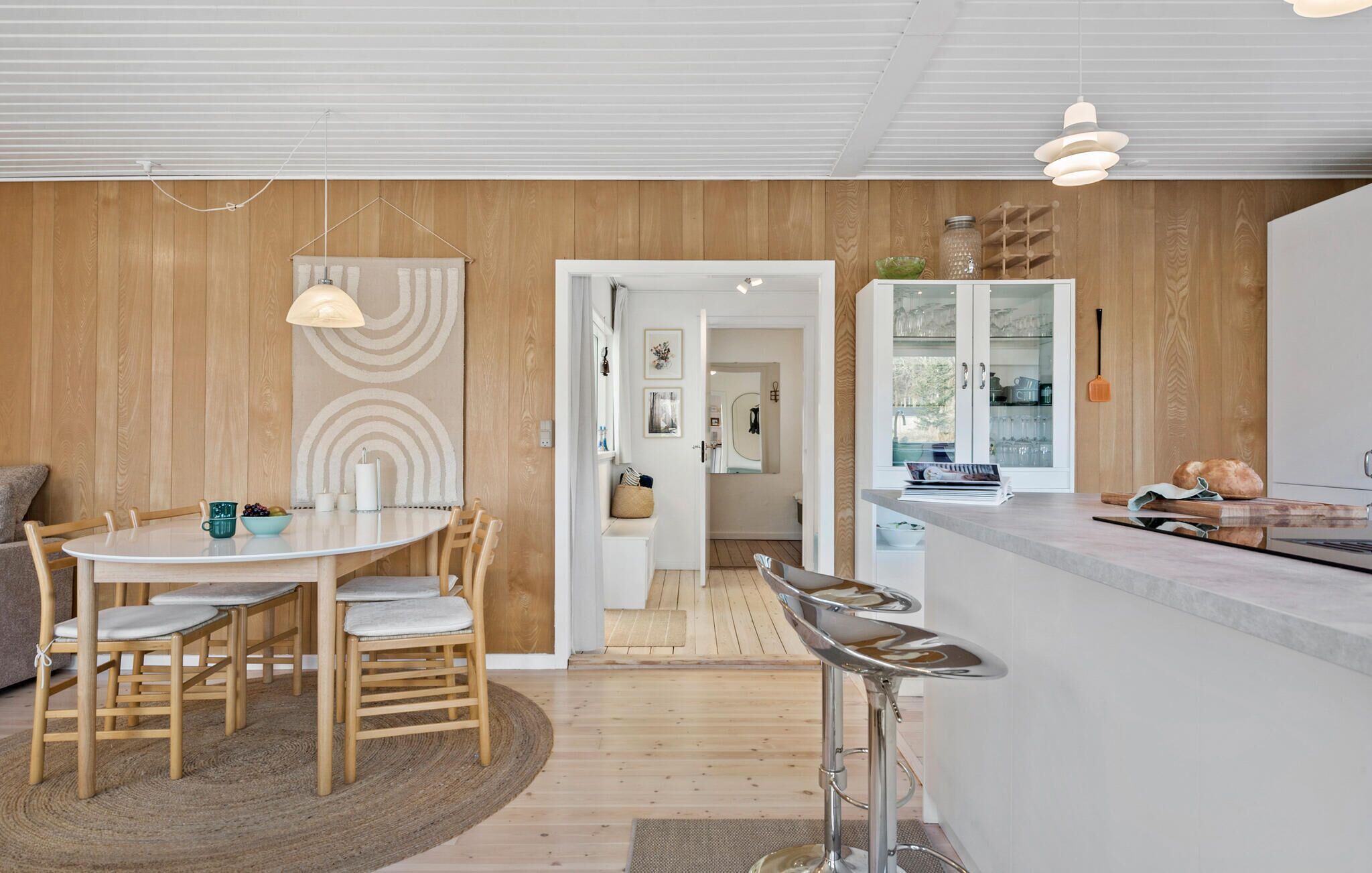 Une cuisine moderne dotée d’un îlot central, de murs recouverts de panneaux en bois et d’un coin repas avec une table ronde et des chaises.