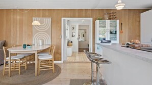 A modern kitchen with a central island, wooden panel walls, and a dining area with a round table and chairs. - 3 bedroom awesome home in Odder (Odder)