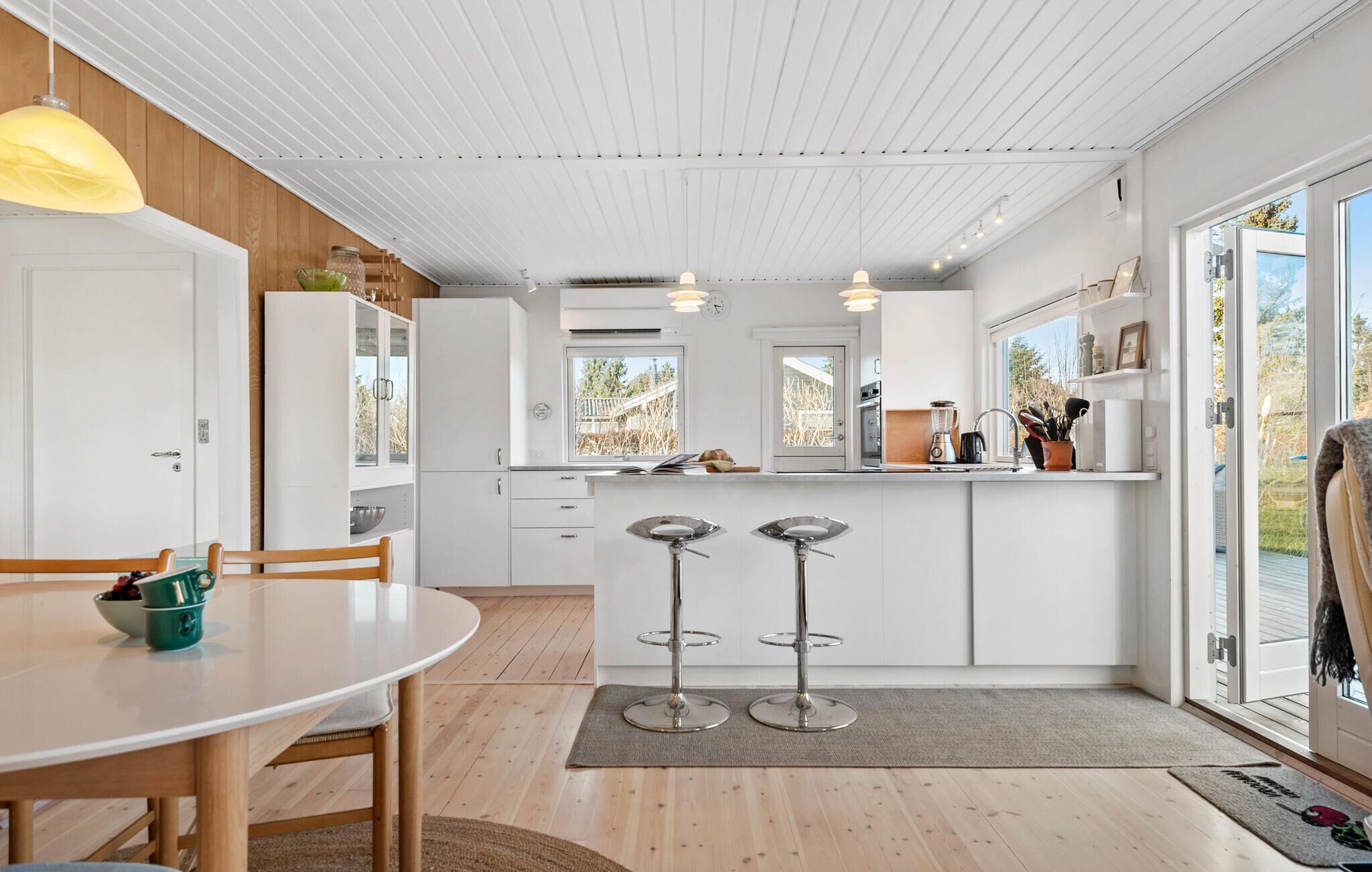 A modern kitchen with white cabinetry, a central island, bar stools, and a dining table.