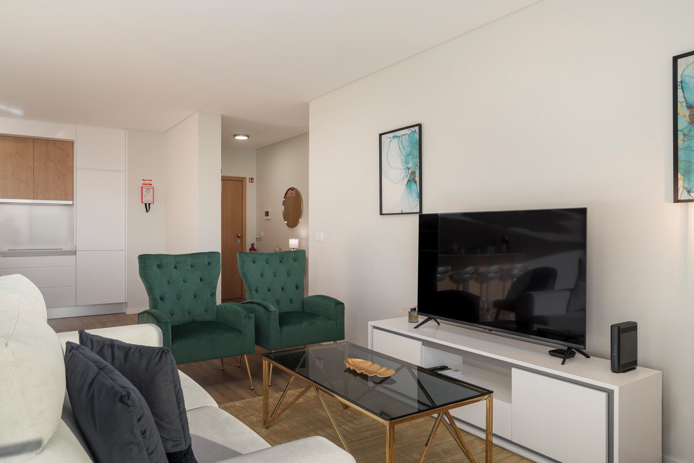 A modern living room with a large flat-screen TV, green upholstered chairs, a glass coffee table, and a white entertainment unit.