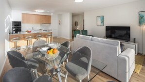 Una sala de estar moderna con una mesa de comedor de cristal, sofás grises y un televisor de pantalla plana.