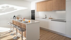 Una cocina moderna con una isla central, taburetes de bar, armarios de madera y electrodomésticos integrados.