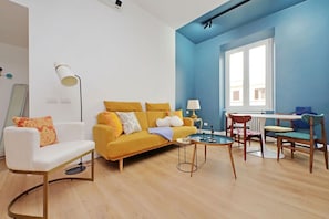 A living room with a yellow sofa, white armchair, and a small table with chairs.