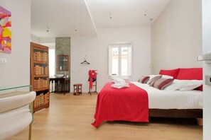 Un dormitorio con cama, armario, una mesita pequeña y un perchero.