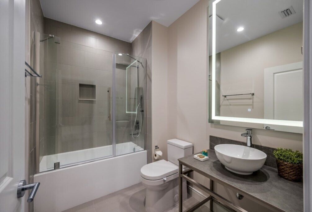 A modern bathroom with a glass-enclosed shower, a white toilet, and a large mirror above a sink with a vessel basin.