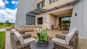 A modern outdoor patio with wicker furniture, a central table with a plant, and a staircase leading to an upper level. - Modern Family Villa Close to Disney & Dining (Kissimmee)