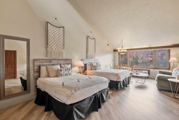 A spacious bedroom with two beds, a large mirror, and a view of the outdoors through a window.