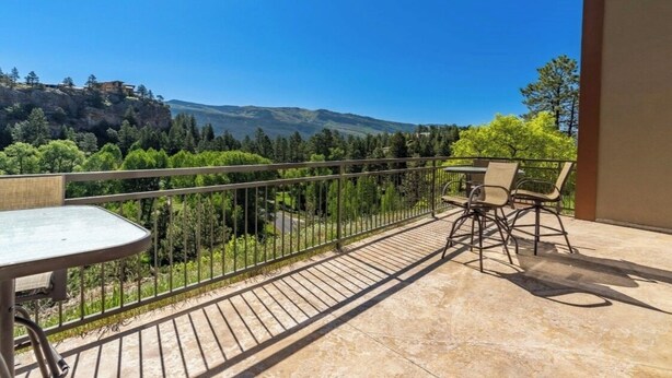 A balcony with a table and chairs, overlooking a mountainous landscape with trees and a building on a cliff. - Luxurious studio condo in lovely Durango, Colorado.  Stay and Play year round. (Durango)