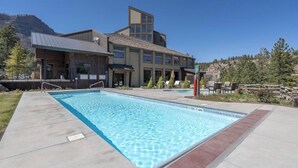A swimming pool with a modern building in the background, surrounded by a landscaped area with trees and a mountain view. - Luxurious studio condo in lovely Durango, Colorado.  Stay and Play year round. (Durango)