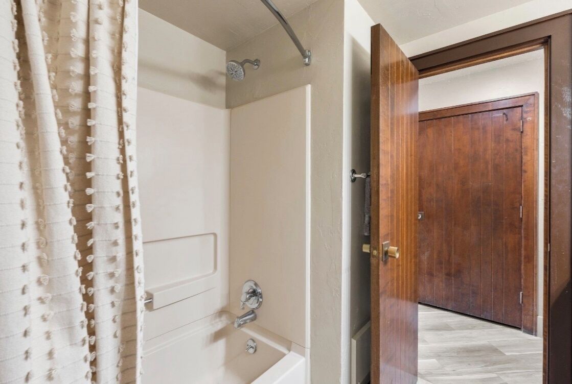 Ein Badezimmer mit Badewanne, Dusche und Holztür.
