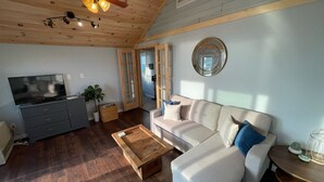 Ein gemütliches Wohnzimmer mit Flachbildfernseher, Couch, Holztisch und Deckenventilator.