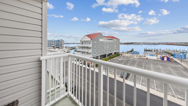 A waterfront view from a balcony with a parking lot, a marina, and a multi-story building with a red roof.