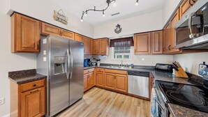 A kitchen with wooden cabinets, stainless steel appliances, a granite countertop, and a black stove.