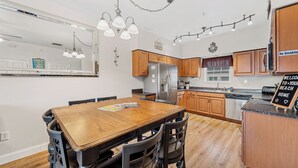 A modern kitchen with wooden cabinets, a stainless steel refrigerator, and a dining area with a wooden table and chairs.
