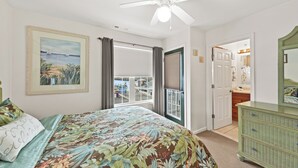 Un dormitorio con cama, ventilador de techo, un cuadro, cómoda y una puerta que da a un balcón.