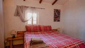 Un dormitorio con una cama, una mesita de noche, una lámpara, una ventana con cortinas y un cuadro en la pared.