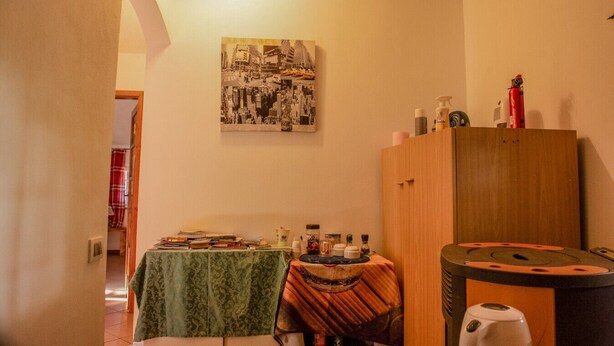 Une pièce avec une table recouverte d’une nappe verte, un meuble en bois et un tableau représentant un paysage urbain accroché au mur.