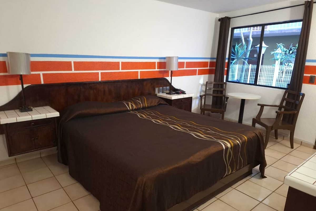 Une chambre d’hôtel avec un grand lit, un bureau, une chaise et une fenêtre donnant sur des palmiers.