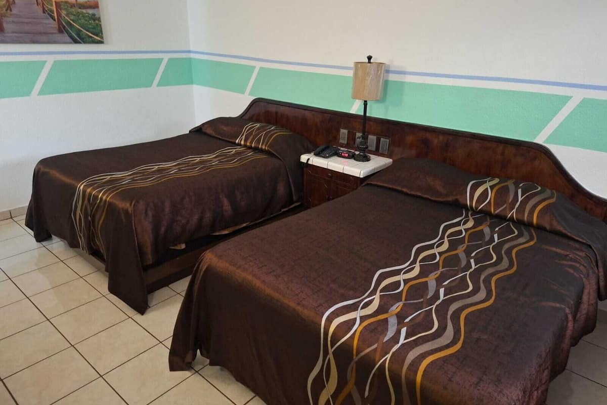 Une chambre avec deux lits, chacun recouvert d’une couverture marron et agrémenté d’un coussin à motifs. On y trouve une table de chevet avec une lampe et un téléphone. La chambre a un sol carrelé et un tableau accroché au mur.