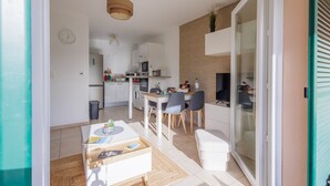 Une cuisine moderne avec des meubles blancs, un coin repas comprenant une table et des chaises, et une porte-fenêtre coulissante donnant sur un balcon.