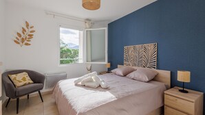 Une chambre à coucher comprenant un lit, une chaise, une table de chevet, une lampe, une fenêtre et un élément de décoration murale.