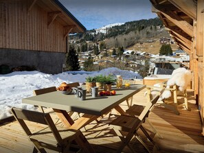 Eine Holzterrasse mit einem für das Frühstück gedeckten Tisch, mit Blick auf ein verschneites Dorf.