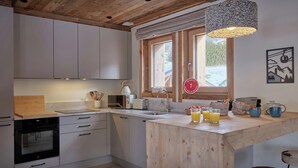 Una cocina moderna con armarios blancos, techo de madera, ventana con vistas y un espacio para desayunar con jugo de naranja y una tetera.