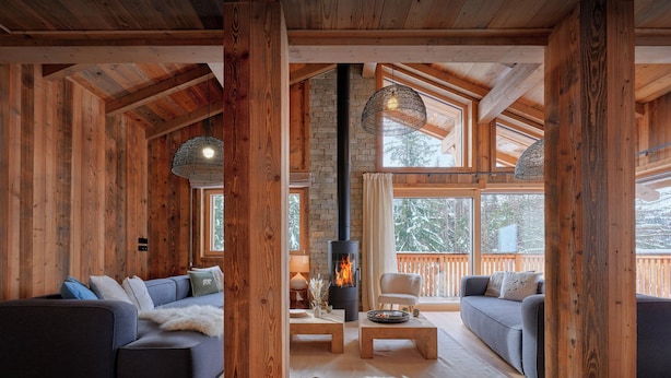 Interior acogedor de una cabaña de troncos con chimenea, vigas de madera y ventanas amplias.