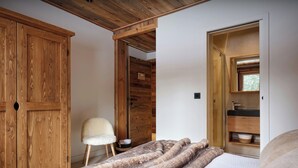 Un dormitorio con un armario de madera, una alfombra mullida, una silla y un baño con lavabo y espejo.