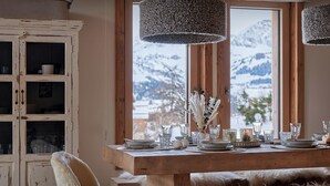Un comedor con una mesa de madera dispuesta para cuatro personas, un armario blanco con puertas de cristal y vistas a montañas nevadas a través de amplios ventanales.