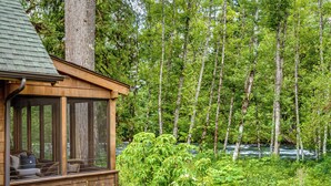 A cabin with a large window overlooking a forested area and a river. -  Cozy, charming two bedroom McKenzie Bridge River front cabin for 2 Guests, (McKenzie Bridge)
