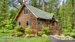 A wooden cabin with a porch, surrounded by a well-maintained garden and trees. -  Cozy, charming two bedroom McKenzie Bridge River front cabin for 2 Guests, (McKenzie Bridge)