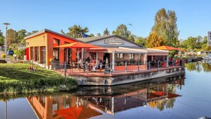 A riverside restaurant with outdoor seating, a covered patio, and a reflection in the water. - 1 bedroom lovely home in Neukalen (Neukalen)
