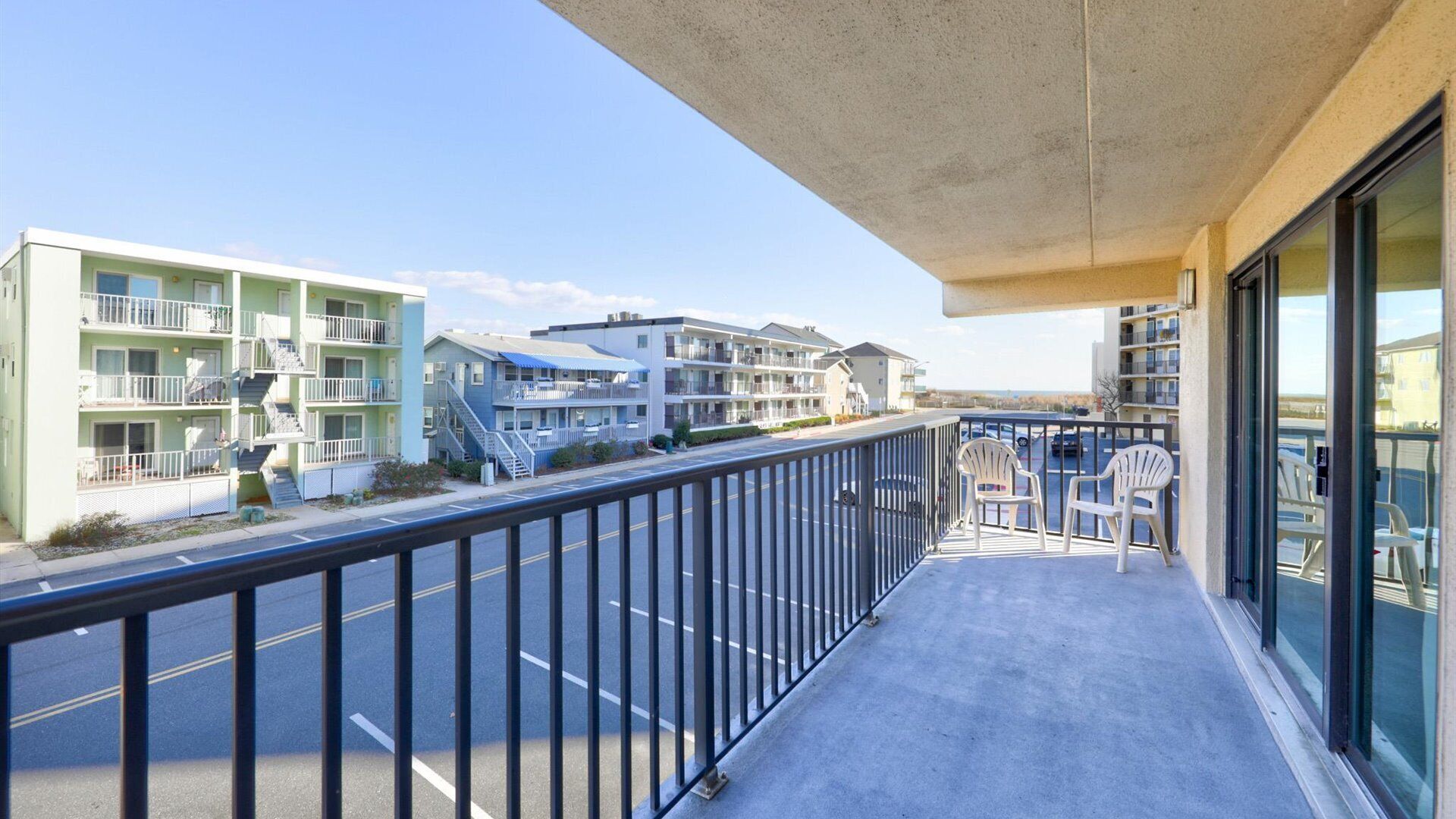 Un balcon donnant sur un immeuble à plusieurs étages, doté de balcons, et sur un parking.