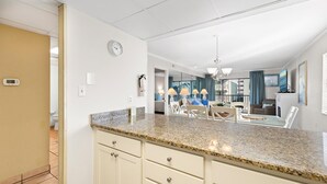 A modern kitchen with granite countertops, a dining area with a glass table, and a living room with a view. - Ocean Time Building - Unit #203 (Ocean City)